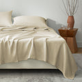 Beige bedding set on a bed with a wooden side table and decorative items.
