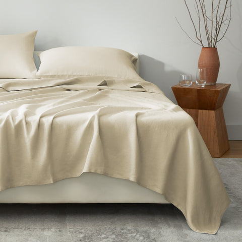 Beige bedding set on a bed with a wooden side table and decorative items.