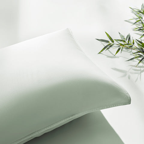 Green pillow on a white surface with a bamboo plant in the corner