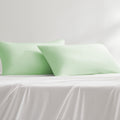 Two cooling green cooling pillowcases on a white bed sheet
