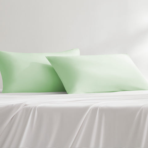 Two cooling green cooling pillowcases on a white bed sheet
