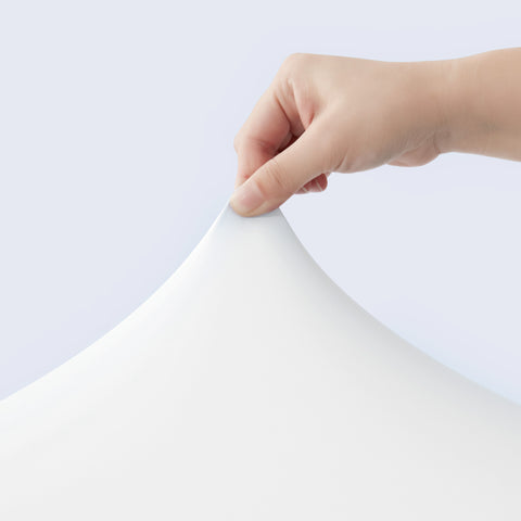 Hand holding a sheet of white cooling fabrics against a light gray background