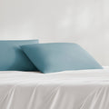Two teal cooling pillowcases on the white bed sheet