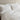 a close-up view of white cotton jersey pillowcase set on a white bed against a neutral wall.